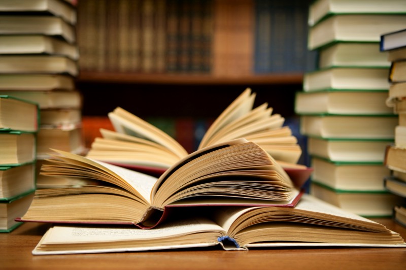 Stack of books with three books open on a library desk.