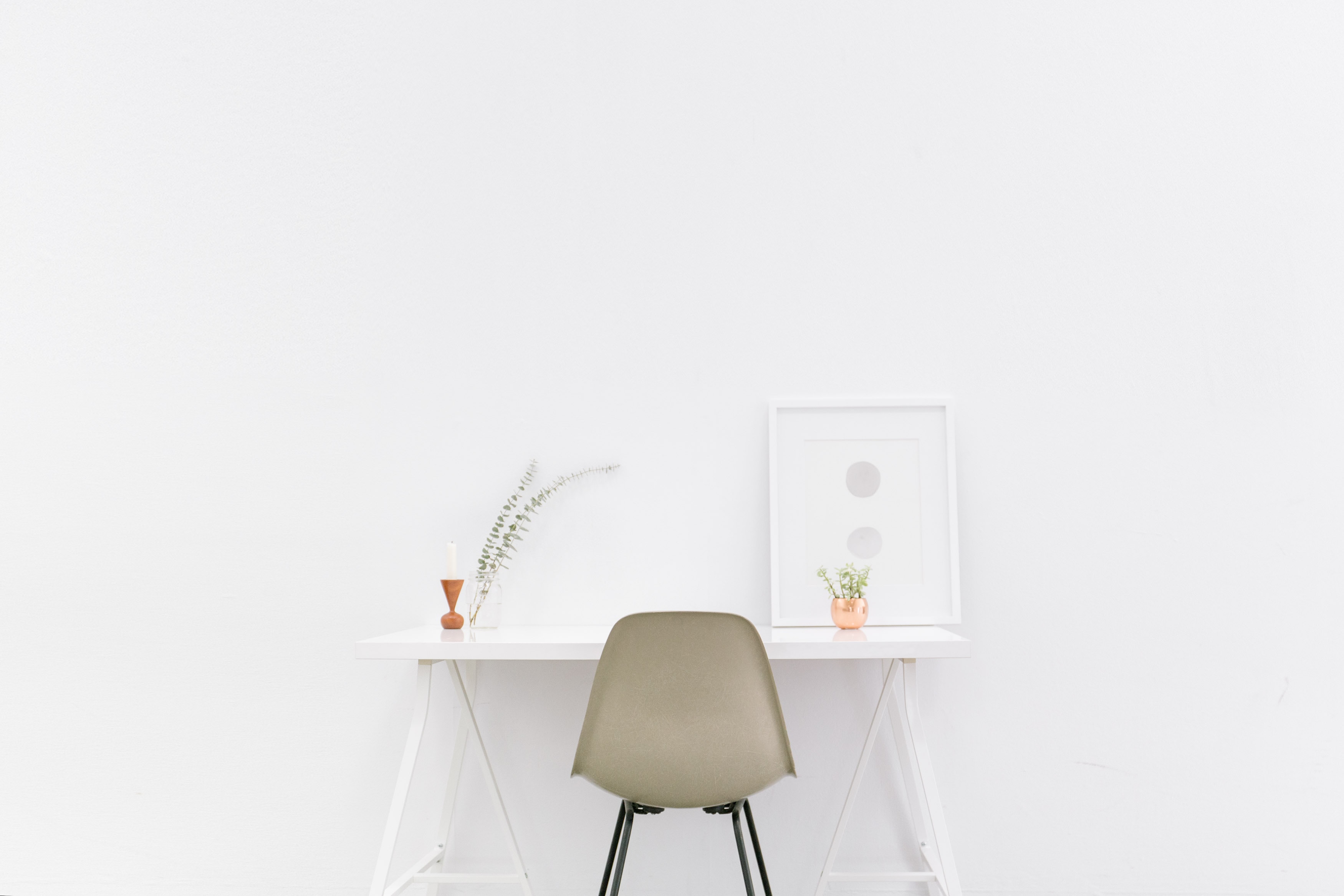 Super white office space with a framed painting and plants adorning the desk.