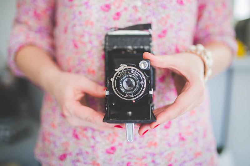 Woman in pink floral shirt holding retro Nikon camera.