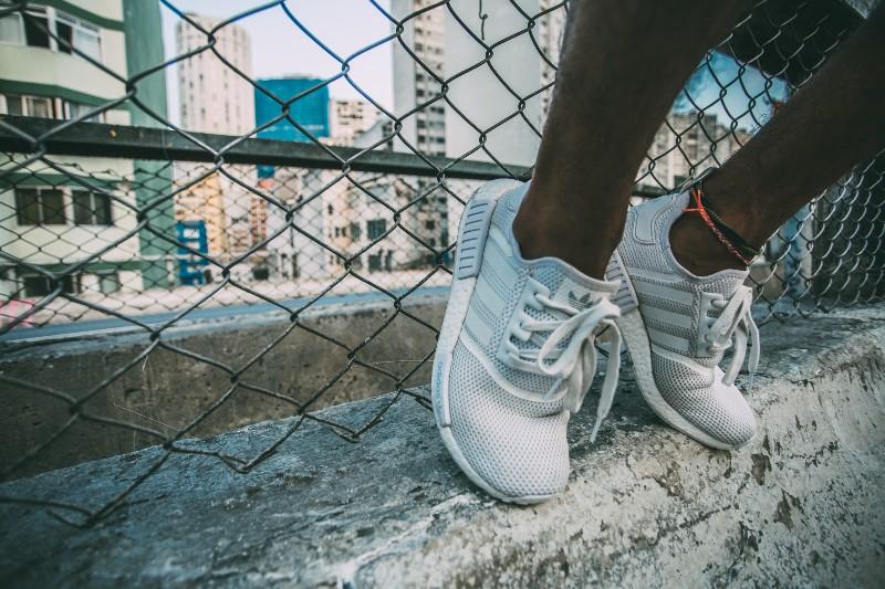 Athlete rests white Adidas shoes on chainlink fence.
