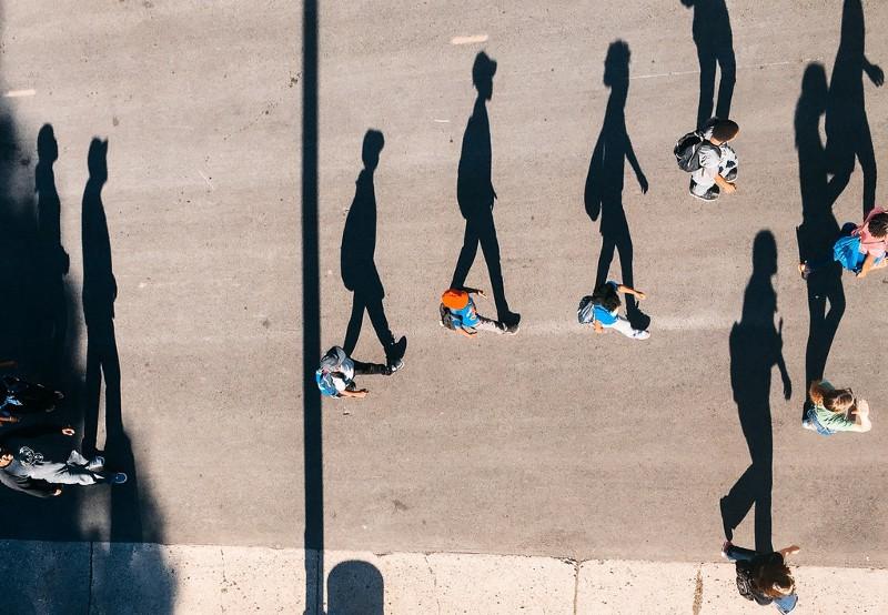 People walking across the street with long shadows.